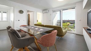 Een moderne woonkamer met een glazen eettafel, comfortabele zithoek, een flatscreen televisie en een balkon met uitzicht.