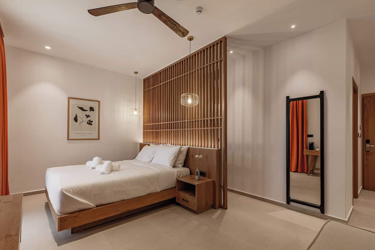 A modern bedroom with a wooden bed frame, a ceiling fan, a bedside table with a lamp, and a framed artwork on the wall.