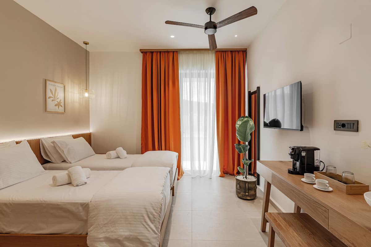 A hotel room with two beds, a ceiling fan, a TV, a coffee machine, and a dining table with cups and a tray.