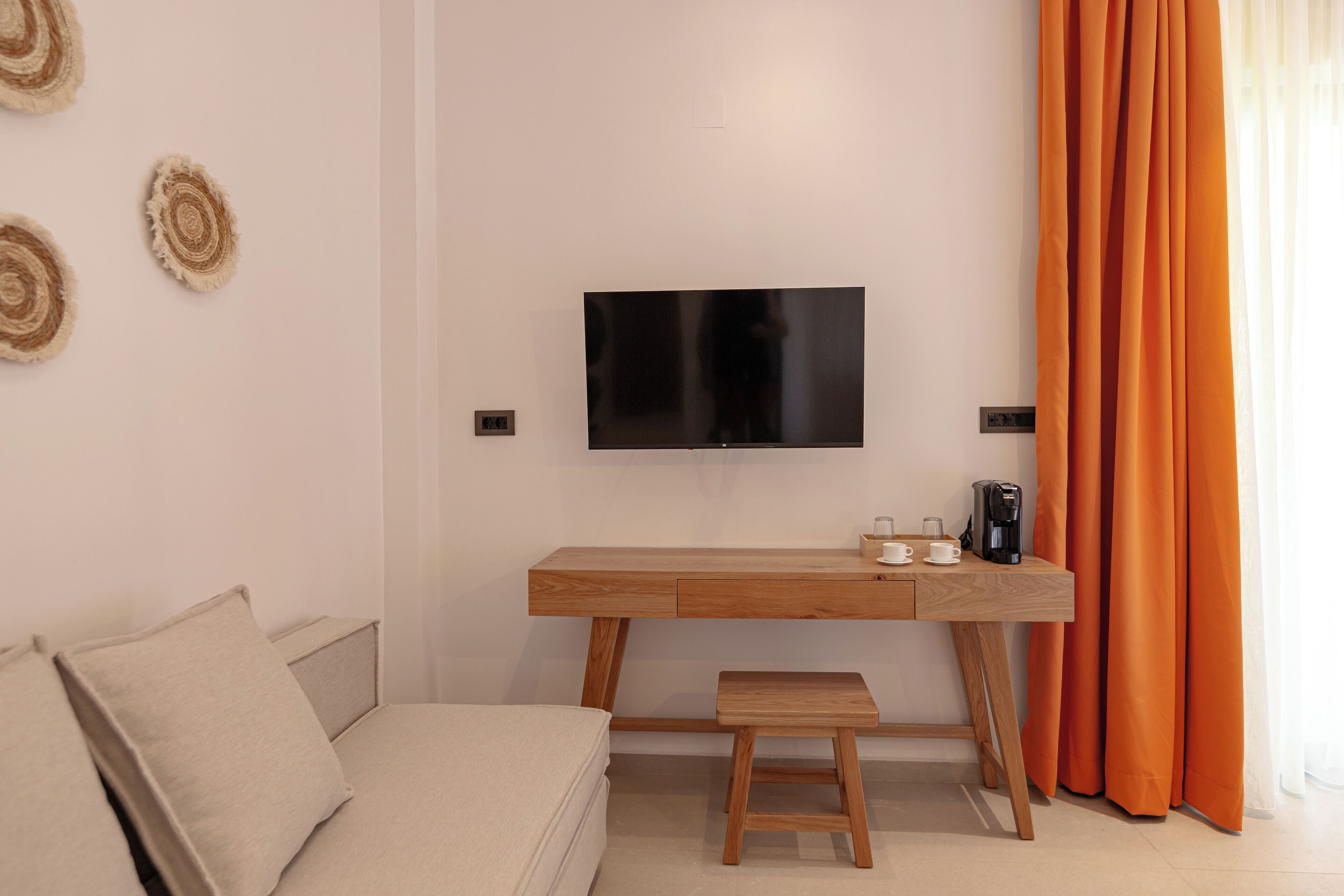 Une chambre moderne avec un bureau en bois, une télévision, une machine à café et une fenêtre ornée de rideaux orange.