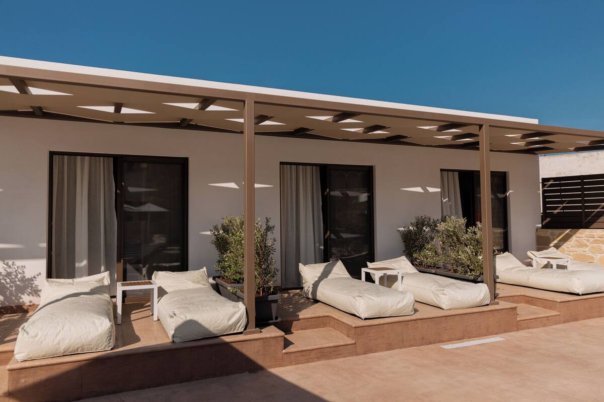 A modern outdoor seating area with built-in benches and cushions, large windows, and a pergola structure.