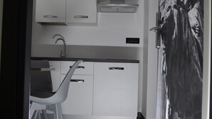 A modern kitchen with white cabinets, a stainless steel countertop, and a single chair.