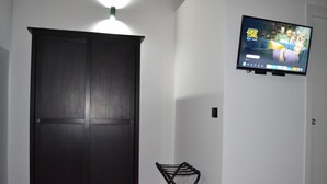A room with a dark wooden wardrobe, a small black metal stool, and a television mounted on the wall displaying 'SpongeBob SquarePants'.