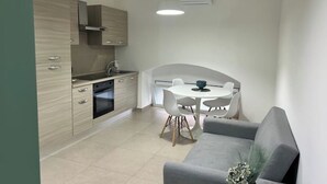 A modern kitchen with light wood cabinets, a built-in oven, and a dining area with a white table and chairs.