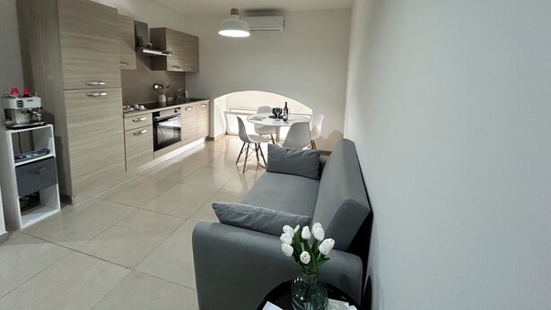 A modern kitchen with a dining area, a sofa, and a vase with flowers.