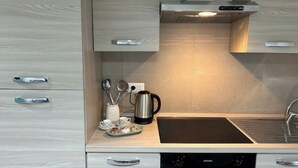 A modern kitchen with light wood cabinetry, a black stovetop, and a stainless steel kettle.