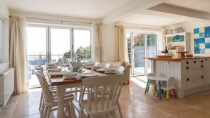 Un comedor luminoso con una mesa grande dispuesta para seis personas, sillas blancas y vistas a un patio exterior a través de puertas de vidrio.