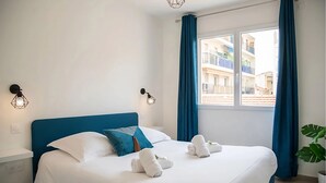 A hotel room with a large bed, blue curtains, and a view of buildings outside. - Comfortable apartment in the heart of Antibes (Antibes)