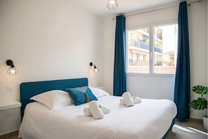 A hotel room with a large bed, blue curtains, and a view of buildings outside.