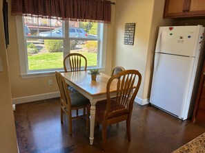 A kitchen with a dining table, chairs, a refrigerator, and a window with a view of the outside.