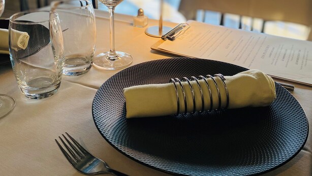 A dining table set with a black placemat, a folded napkin, a fork, a knife, and a glass. - Chambres Dancourt (Charmes)