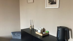 A modern room with a black console table, a grey upholstered chair, a white coffee table, a framed picture, a black coffee maker, and a small bottle of reed diffuser. - Chambres Dancourt (Charmes)