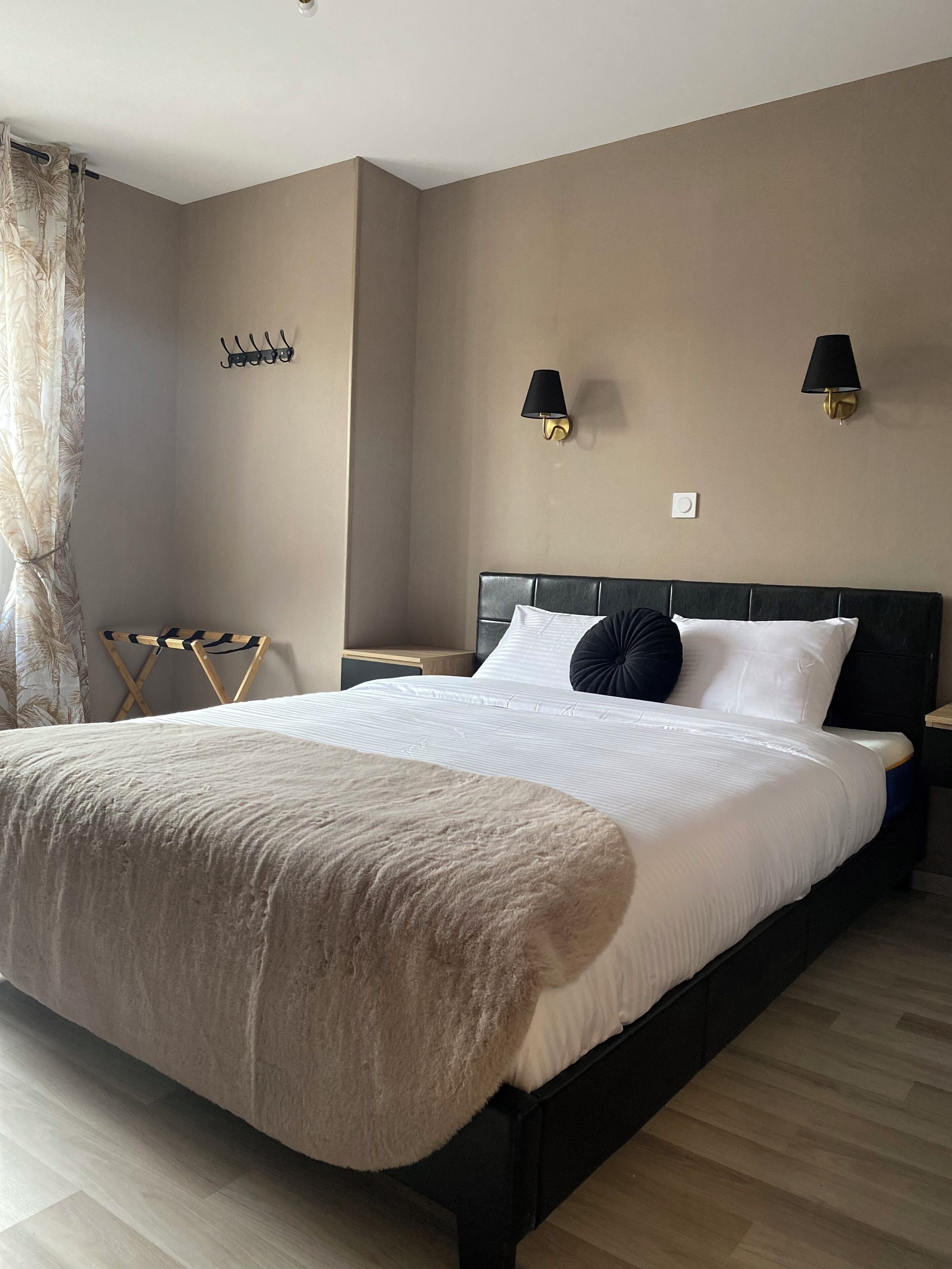 A bedroom with a large bed, two bedside lamps, a nightstand, a wall-mounted lamp, and a coat rack.