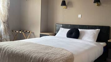 A bedroom with a large bed, two bedside lamps, a nightstand, a wall-mounted lamp, and a coat rack.