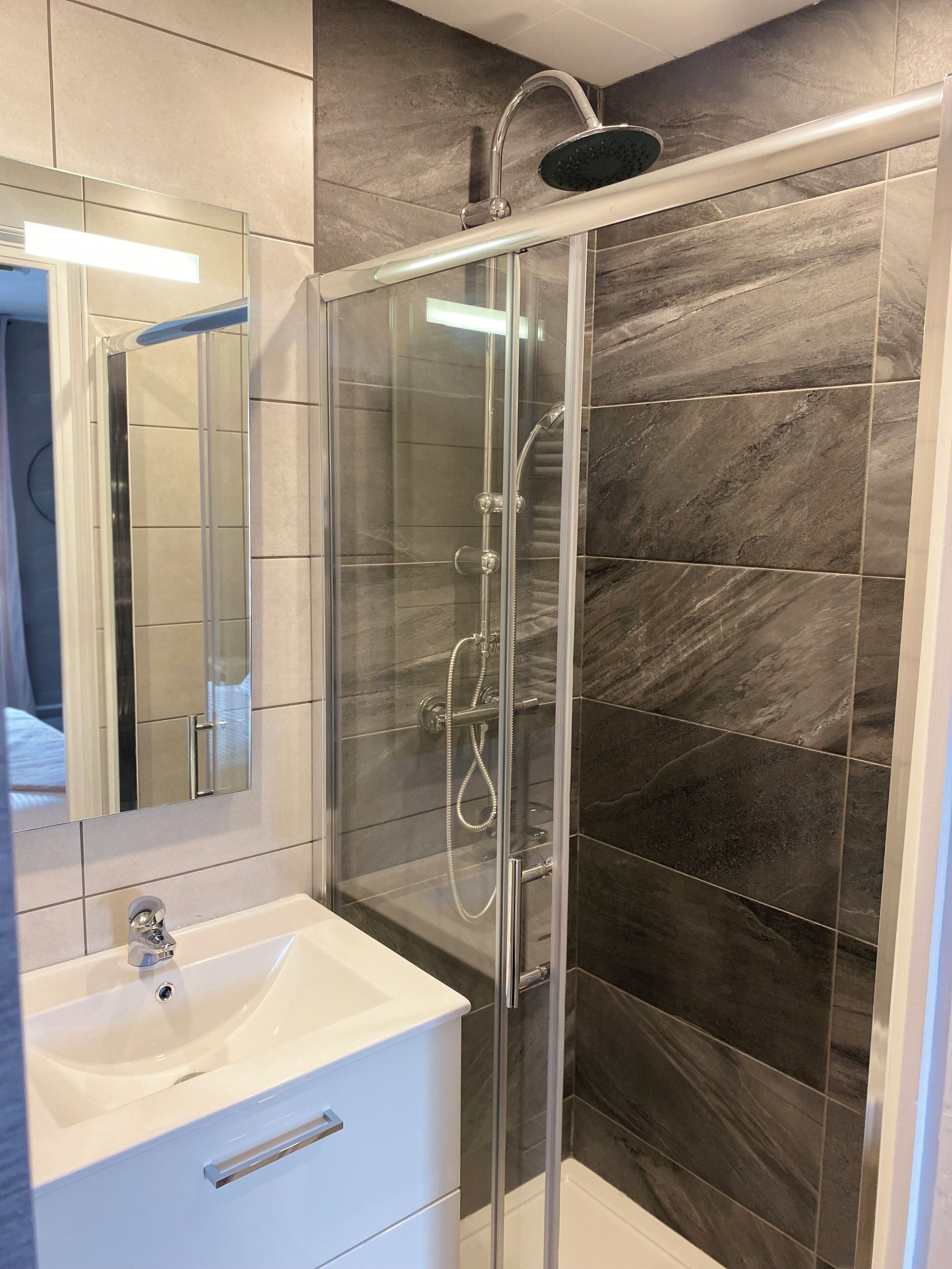 Une salle de bain moderne avec une douche à parois de verre, un lavabo blanc et un grand miroir.