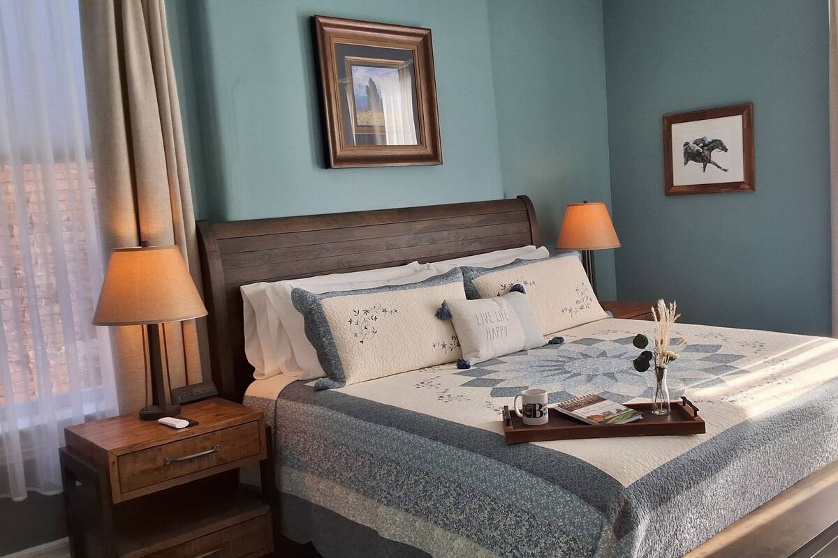 A neatly made bed with a patterned bedspread, two bedside lamps, and a tray with a mug and a book.