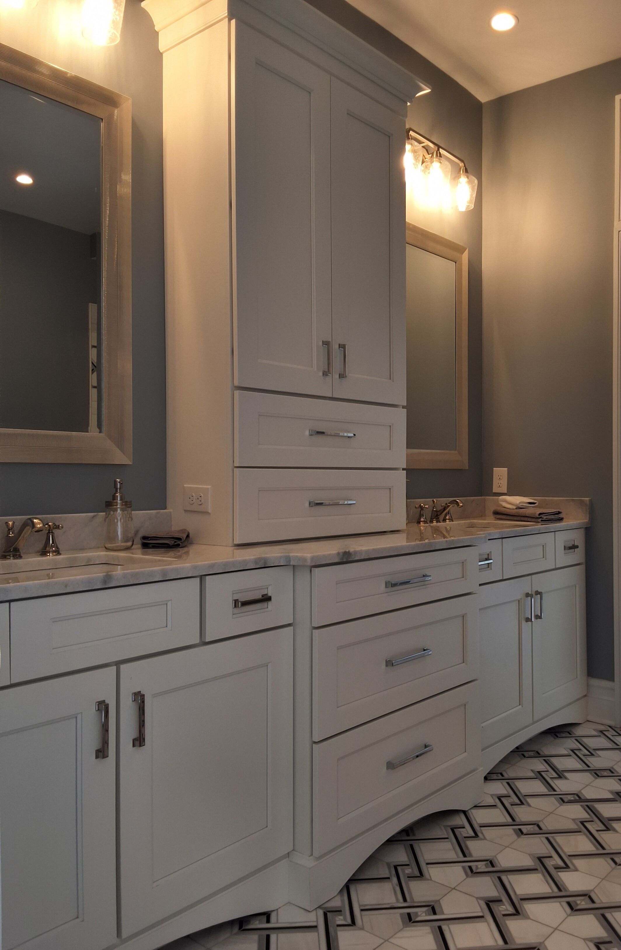 A modern bathroom with white cabinetry, a large mirror, and a patterned floor.