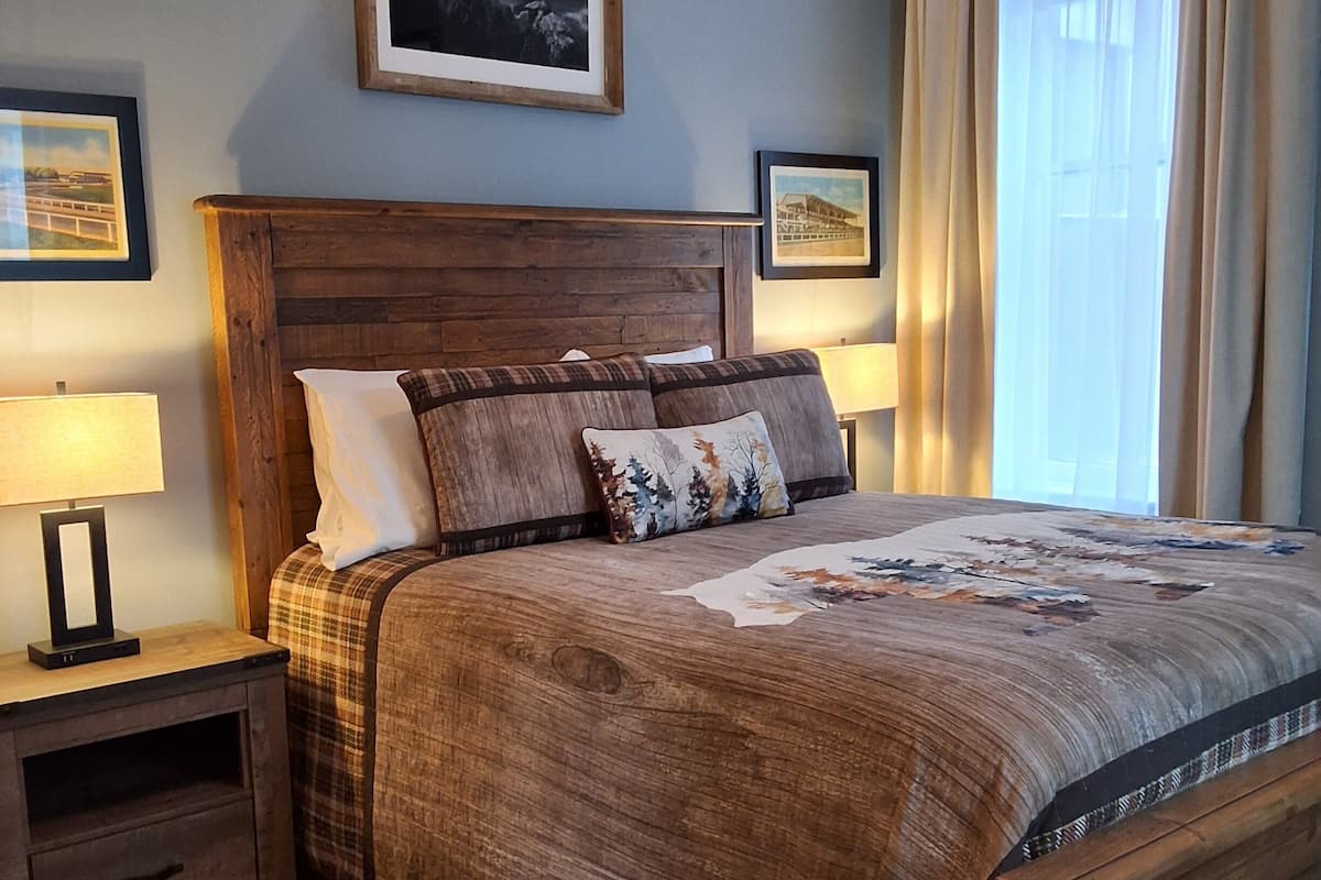 A bedroom with a wooden bed, two bedside tables, a nightstand, a patterned rug, and two framed pictures on the wall.