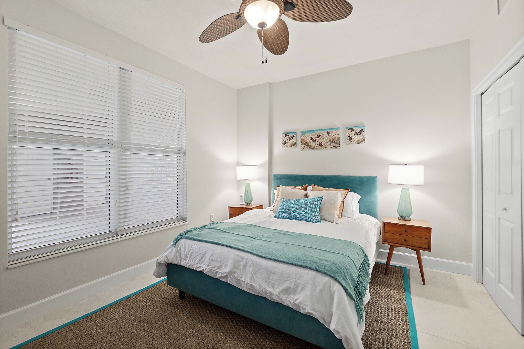 A bedroom with a bed, two bedside tables with lamps, a ceiling fan, and a window with blinds.