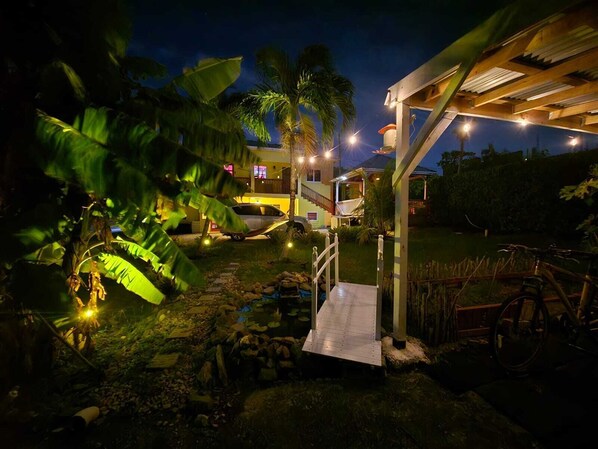 A well-lit outdoor area with a wooden structure, a pathway leading to a building, and a bicycle.