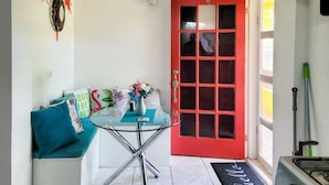 A small, bright room with a red door, a glass table with a vase of flowers, teal cushions, and a welcome mat. - Genesis King Suite Apt 4 located in peaceful valley AC, Wi-Fi, King Bed (Cassada Gardens)
