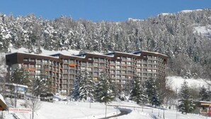 Un hôtel à plusieurs étages, doté d’une architecture moderne, entouré d’arbres couverts de neige et surplombant un ciel bleu clair.