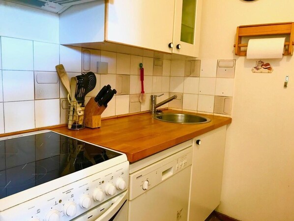 A kitchen with white cabinets, a wooden countertop, a stove, a dishwasher, and a sink.