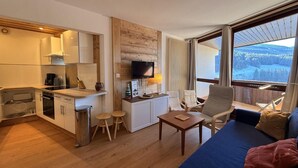 Un espace de vie compact comprenant un coin cuisine, un coin repas et un espace détente avec vue sur un paysage enneigé.