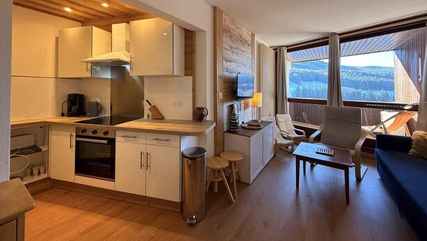 Un espace de vie compact comprenant un coin cuisine, un coin repas et un espace détente avec vue.