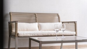 A wicker sofa with cushions, a glass coffee table, and two empty wine glasses on the table. - GuestReady - Acqua residences - Aquamarine (Funchal)
