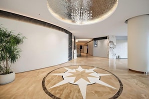 Eine Hotelhalle mit einem großen Sternmuster auf dem Boden, einer Zimmerpflanze und einem modernen Kronleuchter.