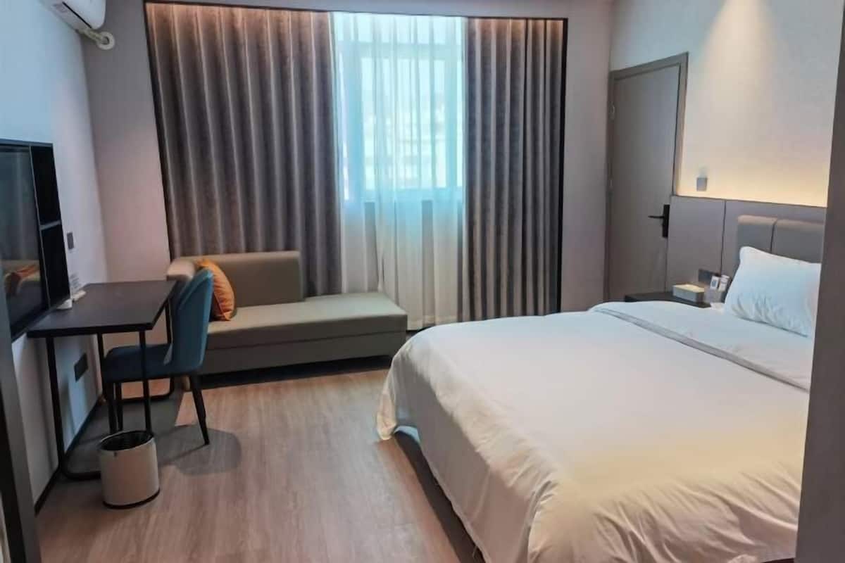 Ein Hotelzimmer mit Bett, Schreibtisch, Stuhl, Sofa und einem Fenster mit Vorhängen.