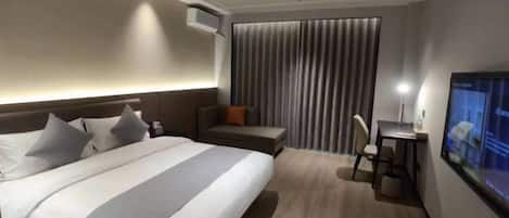 A hotel room with a bed, a desk, a chair, a TV, and a window with curtains.