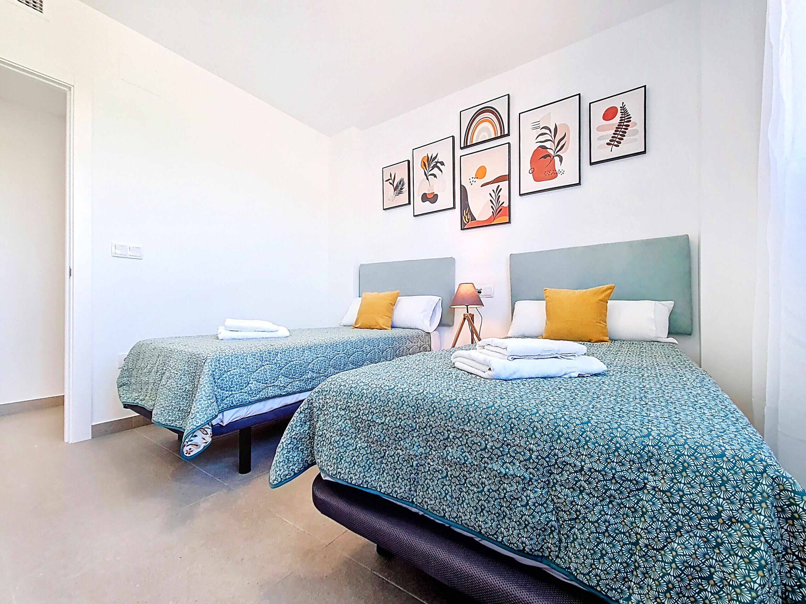 Two beds with patterned bedspreads, a bedside lamp, and artwork on the wall.