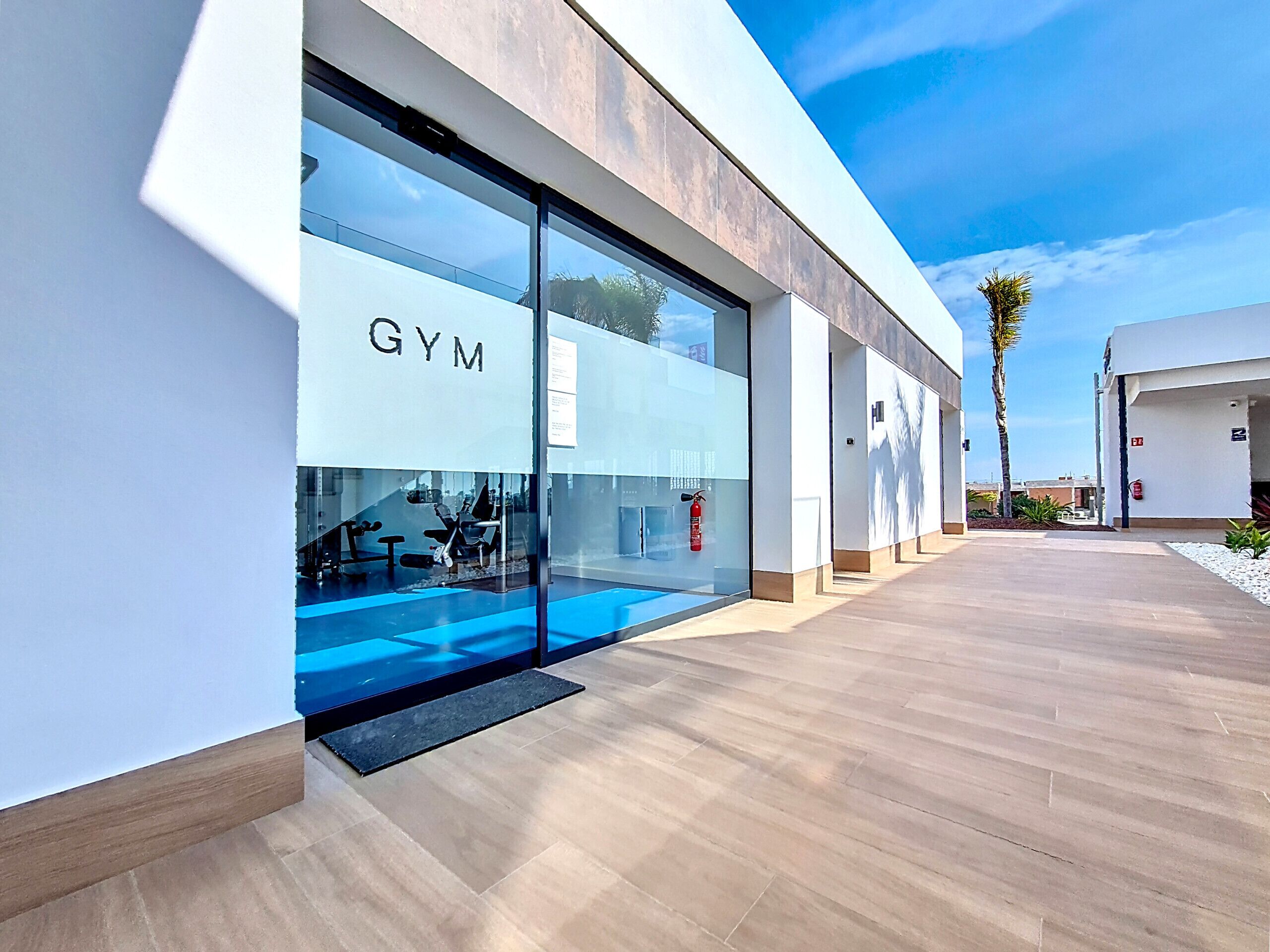 A modern gym with glass walls, a fire extinguisher, and a clear sky.