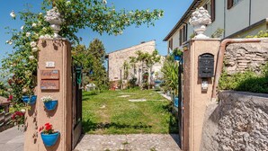 A narrow pathway leading to a building with a stone facade, a blue flower pot, and a sign with room names.