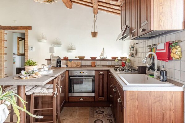 Una cocina con gabinetes de madera, horno empotrado y encimera con distintos utensilios de cocina.