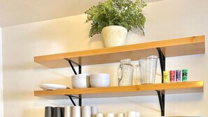 Une cuisine avec des armoires bleues, un plan de travail en bois, un évier, un mixeur et des étagères où sont rangés de la vaisselle et une plante.