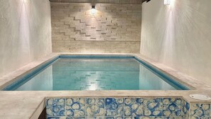Une piscine rectangulaire bordée de carreaux et dont le mur, situé derrière, est décoré d’un motif en briques.
