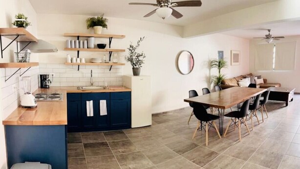 Une cuisine moderne avec des meubles de couleur bleu foncé, un plan de travail en bois et un coin repas comprenant une grande table et des chaises.