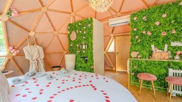 A cozy, well-lit room with a bed adorned with rose petals, a wooden ceiling, and a green wall with flowers.