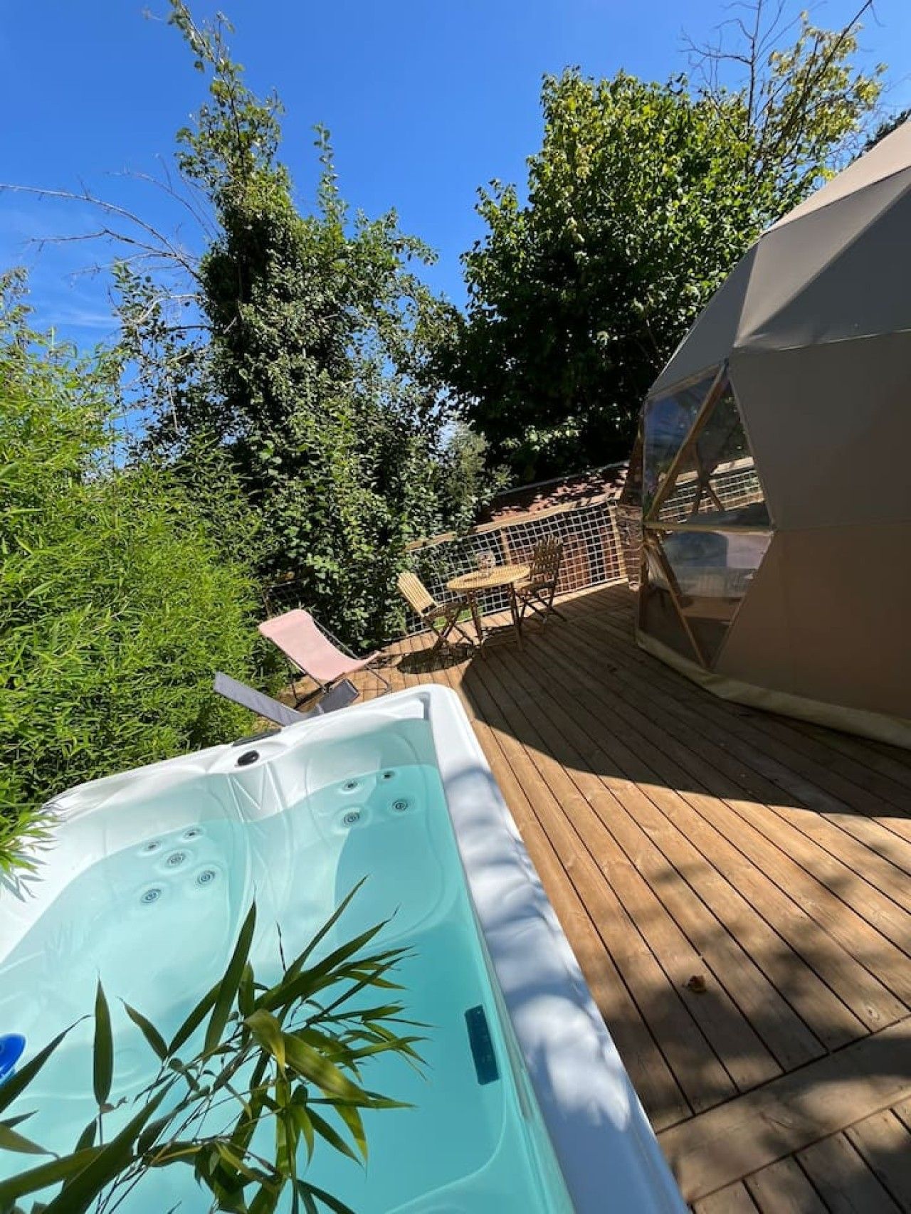 Un bain à remous sur une terrasse en bois, avec vue sur les arbres et une structure en forme de dôme géodésique.