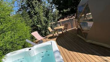Un bain à remous sur une terrasse en bois, avec vue sur les arbres et une structure en forme de dôme géodésique.