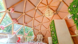 A room with a geometric wooden ceiling, a bed with rose petals, and a green wall with flowers.