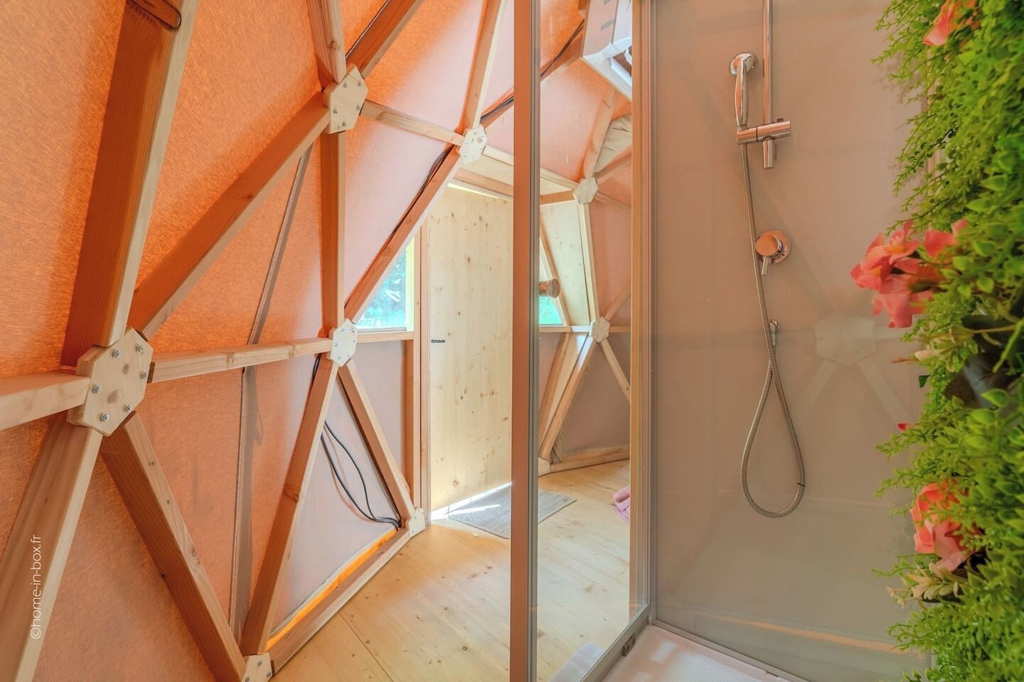 A room with a wooden ceiling structure, a shower with a handheld hose, and a view of an adjacent room.