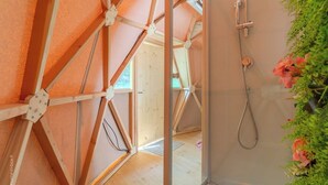 A room with a wooden ceiling structure, a shower with a handheld hose, and a view of an adjacent room.