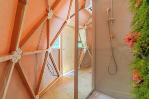 Una habitación con estructura de techo de madera, ducha con manguera de mano y vista a una habitación contigua.