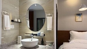 Un baño moderno con un espejo redondo, un lavabo blanco y una cama con ropa de cama blanca.