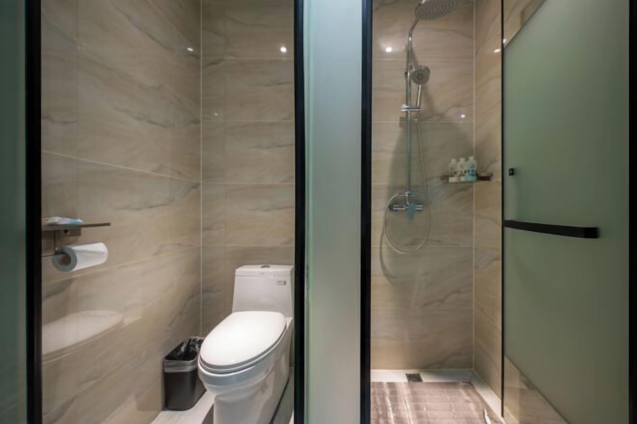 Une salle de bain moderne avec une douche à parois de verre, des toilettes et un rouleau de papier toilette posé sur une étagère.
