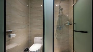 Un baño moderno con ducha de vidrio, un inodoro y un rollo de papel higiénico en un estante.